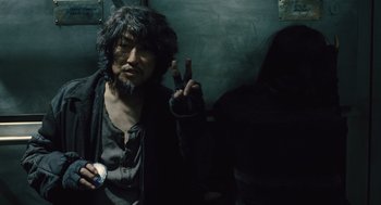 Movie still from “Snowpiercer” (2013), directed by Bong Joon Ho – A man with long black hair is making a peace sign; Medium shot, Over the shoulder angle