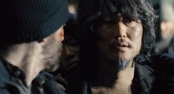 Movie still from “Snowpiercer” (2013), directed by Bong Joon Ho – A man with long black hair and a beard is standing next to another man with long black hair and a beard; Close Up shot, Over the shoulder angle
