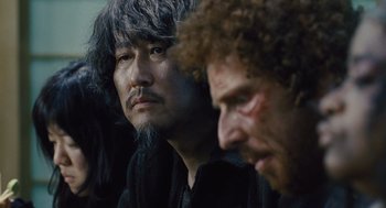 Movie still from “Snowpiercer” (2013), directed by Bong Joon Ho – A man with long hair and a gray beard is sitting next to another man with curly hair; Close Up shot, Over the shoulder angle