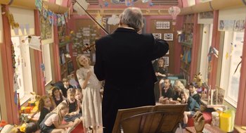 Movie still from “Snowpiercer” (2013), directed by Bong Joon Ho – An older man playing a violin in front of an audience; Wide shot, Low angle