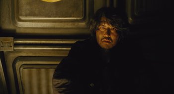 Movie still from “Snowpiercer” (2013), directed by Bong Joon Ho – A man with long black hair and a black jacket; Close Up shot, Low angle