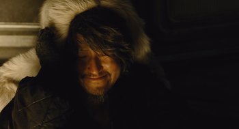 Movie still from “Snowpiercer” (2013), directed by Bong Joon Ho – A man wearing a fur hat and smiling for the camera; Close Up shot, High angle