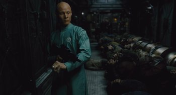 Movie still from “Snowpiercer” (2013), directed by Bong Joon Ho – A bald man in a blue robe standing next to a group of people; Medium shot, High angle