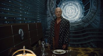 Movie still from “Snowpiercer” (2013), directed by Bong Joon Ho – A man standing in front of a plate of food in a room; Medium shot, Low angle