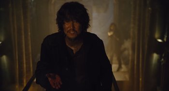 Movie still from “Snowpiercer” (2013), directed by Bong Joon Ho – A man with long black hair is standing in a dark room; Medium shot, Over the shoulder angle