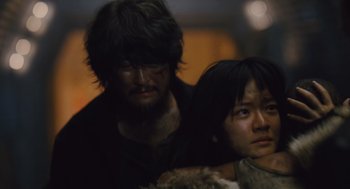 Movie still from “Snowpiercer” (2013), directed by Bong Joon Ho – A man standing next to a woman in a dark room; Close Up shot, Over the shoulder angle