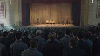 Movie still from “So Long, My Son” (2019), directed by Xiaoshuai Wang – A group of people sitting at a table in front of an audience; Extreme Wide shot, High angle