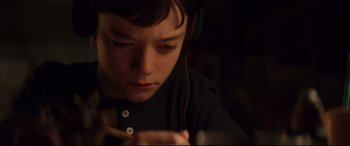 Movie still from “A Monster Calls” (2016), directed by J.A. Bayona – A young boy wearing headphones looking down at his cell phone; Close Up shot, High angle