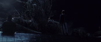 Movie still from “A Monster Calls” (2016), directed by J.A. Bayona – A boy standing in front of a tree in a dark room; Wide shot, Over the shoulder angle