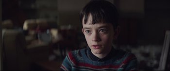 Movie still from “A Monster Calls” (2016), directed by J.A. Bayona – A young boy wearing a striped sweater stares into the camera; Close Up shot, Over the shoulder angle