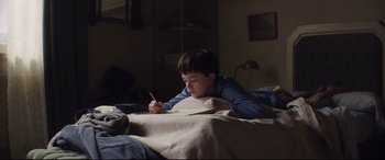 Movie still from “A Monster Calls” (2016), directed by J.A. Bayona – A young boy is writing in a notebook; Medium shot, High angle