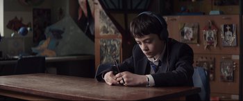 Movie still from “A Monster Calls” (2016), directed by J.A. Bayona – A young boy wearing headphones looking at a cell phone; Medium shot, High angle