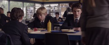 Movie still from “A Monster Calls” (2016), directed by J.A. Bayona – Two young men sitting at a table in front of yellow plates; Medium shot, Over the shoulder angle