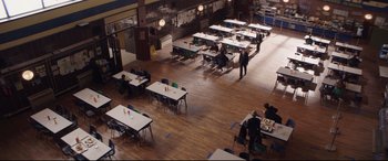 Movie still from “A Monster Calls” (2016), directed by J.A. Bayona – People are sitting at tables in an empty room; Extreme Wide shot, High angle