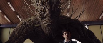 Movie still from “A Monster Calls” (2016), directed by J.A. Bayona – A young boy standing next to a large tree; Medium shot, Low angle