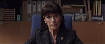 Movie still from “A Monster Calls” (2016), directed by J.A. Bayona – An older woman sitting on a blue chair in an office setting; Close Up shot, High angle