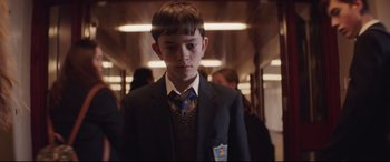 Movie still from “A Monster Calls” (2016), directed by J.A. Bayona – A boy in a suit and tie standing in front of a crowd; Medium shot, Low angle
