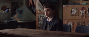 Movie still from “A Monster Calls” (2016), directed by J.A. Bayona – A boy in a suit sitting at a table in a restaurant; Medium shot, High angle