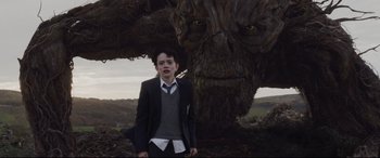 Movie still from “A Monster Calls” (2016), directed by J.A. Bayona – A young boy standing in front of a large tree; Medium shot, Low angle