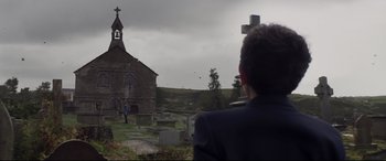 Movie still from “A Monster Calls” (2016), directed by J.A. Bayona – A man standing in front of an old stone church; Extreme Wide shot, Over the shoulder angle