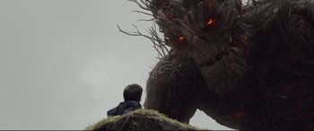 Movie still from “A Monster Calls” (2016), directed by J.A. Bayona – A man sitting on top of a hill next to a giant tree; Wide shot, Low angle