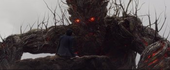 Movie still from “A Monster Calls” (2016), directed by J.A. Bayona – A man sitting on top of a tree next to a tree with eyes glowing; Wide shot, Over the shoulder angle