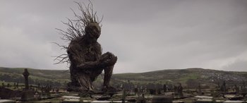 Movie still from “A Monster Calls” (2016), directed by J.A. Bayona – A statue of a man sitting in a field; Wide shot, Low angle