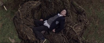 Movie still from “A Monster Calls” (2016), directed by J.A. Bayona – A boy in a suit laying on a pile of tree branches; Medium shot, Overhead angle