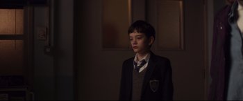 Movie still from “A Monster Calls” (2016), directed by J.A. Bayona – A boy in a suit and tie standing in front of a window; Medium shot, Over the shoulder angle