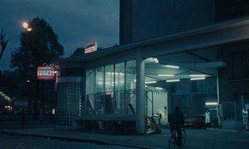 Movie still from “So Long, Stooge” (1983), directed by Claude Berri – A person riding a bike in front of a building; Extreme Wide shot, Low angle