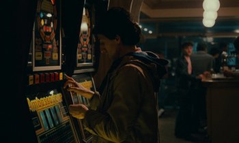 Movie still from “So Long, Stooge” (1983), directed by Claude Berri – A man standing in front of a slot machine at night; Medium shot, Over the shoulder angle