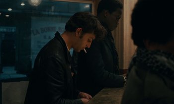 Movie still from “So Long, Stooge” (1983), directed by Claude Berri – A man sitting at a bar smoking a cigarette; Medium shot, Over the shoulder angle