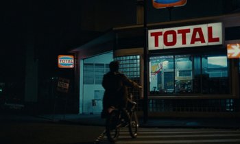 Movie still from “So Long, Stooge” (1983), directed by Claude Berri – A man riding a bike down a street at night; Extreme Wide shot, High angle