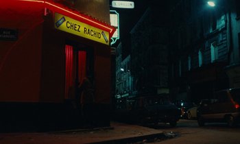 Movie still from “So Long, Stooge” (1983), directed by Claude Berri – A street sign on the side of a building at night; Extreme Wide shot, Over the shoulder angle