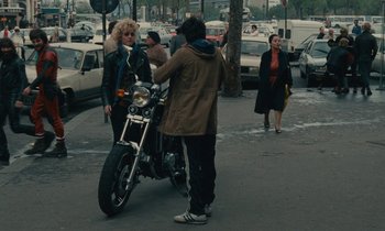 Movie still from “So Long, Stooge” (1983), directed by Claude Berri – A man is standing next to a motorcycle on the street; Wide shot, High angle