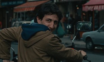 Movie still from “So Long, Stooge” (1983), directed by Claude Berri – A man riding a motorcycle down a street; Close Up shot, Over the shoulder angle