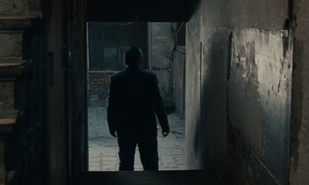 Movie still from “So Long, Stooge” (1983), directed by Claude Berri – A man standing in a dark alleyway with his hands in his pockets; Wide shot, High angle