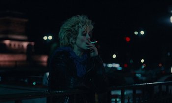 Movie still from “So Long, Stooge” (1983), directed by Claude Berri – A woman smoking a cigarette while standing on a bridge; Medium shot, Over the shoulder angle