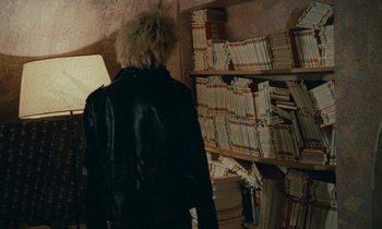 Movie still from “So Long, Stooge” (1983), directed by Claude Berri – A person standing in front of a book shelf; Medium shot, Over the shoulder angle