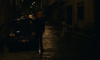 Movie still from “So Long, Stooge” (1983), directed by Claude Berri – A woman standing on the side of a street at night; Wide shot, High angle