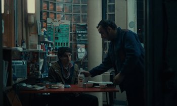 Movie still from “So Long, Stooge” (1983), directed by Claude Berri – Two men are sitting at a table in a store; Medium shot, Over the shoulder angle
