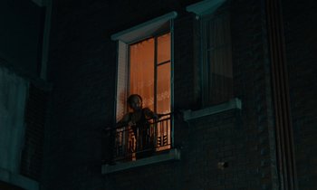 Movie still from “So Long, Stooge” (1983), directed by Claude Berri – A person standing on a balcony at night looking out of a window; Extreme Wide shot, Low angle