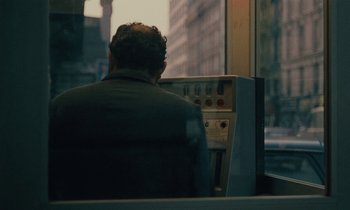 Movie still from “So Long, Stooge” (1983), directed by Claude Berri – A man sitting in front of an atm machine on a bus; Medium shot, Over the shoulder angle
