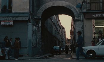 Movie still from “So Long, Stooge” (1983), directed by Claude Berri – An old archway leads to an alley way in an urban setting; Extreme Wide shot, Over the shoulder angle