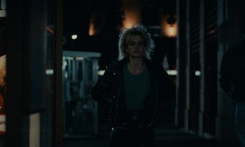 Movie still from “So Long, Stooge” (1983), directed by Claude Berri – A woman in a leather jacket standing on a sidewalk; Medium shot, Low angle