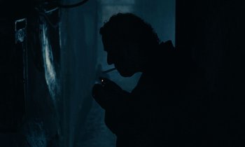 Movie still from “So Long, Stooge” (1983), directed by Claude Berri – A man smoking a cigarette in a dark room; Close Up shot, Low angle