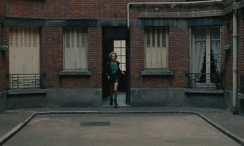 Movie still from “So Long, Stooge” (1983), directed by Claude Berri – A woman standing in front of a brick building; Wide shot, Over the shoulder angle