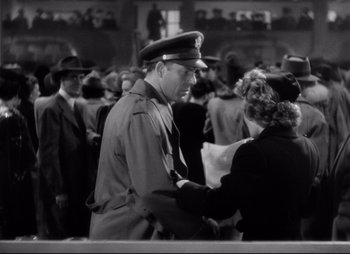 Movie still from “So Proudly We Hail” (1990), directed by Lionel Chetwynd – An old photo of a man and a woman in a crowd; Medium shot, Low angle