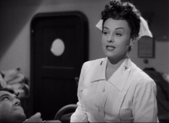 Movie still from “So Proudly We Hail” (1990), directed by Lionel Chetwynd – An old photo of a woman wearing a white suit; Medium shot, High angle