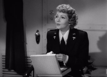 Movie still from “So Proudly We Hail” (1990), directed by Lionel Chetwynd – An old photo of a woman sitting at a table with a laptop; Medium shot, Low angle